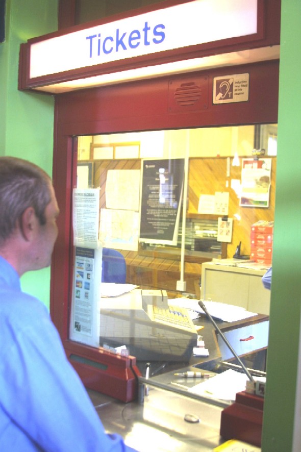 A man is purchasing tickets at a ticket window. A sign above the window indicates telecoil service is available.