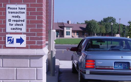 A car at a bank drive-through. A sign indicates telecoil service is present.